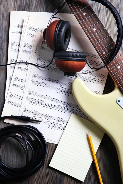 Electric guitar with headphones and musical notes on wooden background