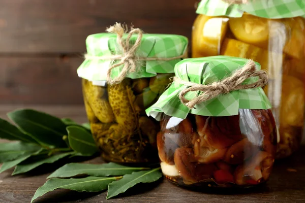 Jars with pickled vegetables and mushrooms on wooden background