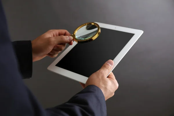 Businessman holding magnifying glass and digital table