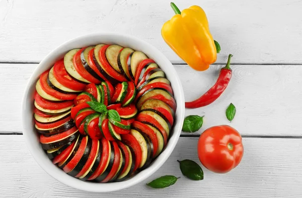 Ratatouille, stewed vegetable dish with tomatoes, zucchini, eggplant before cooking in pan, on wooden background