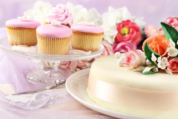 Cake with sugar paste flowers and cupcakes, on light background
