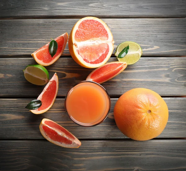 Glass of grapefruit juice and fresh fruits on wooden background