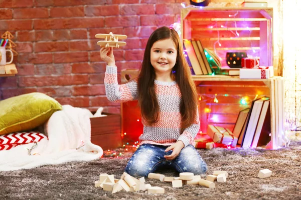 Pretty little girl playing with wooden plane in Christmas decorated room