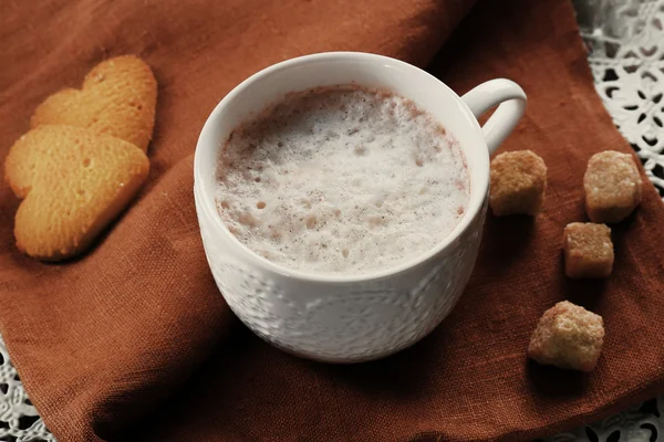 Cup of hot cacao with heart shaped cookies on brown cotton serviette