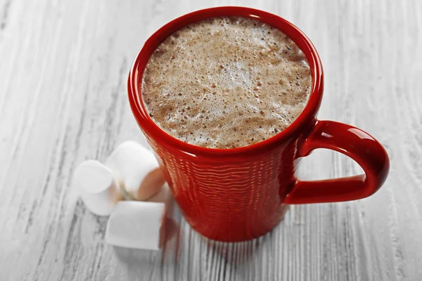 Red cup of hot cacao and marshmallow on wooden background
