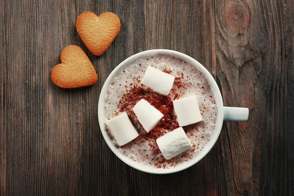 Cup of hot cacao with marshmallow and heart shaped cookies on wooden background
