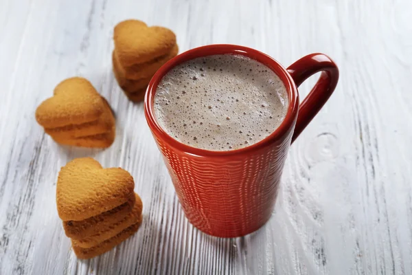 Red cup of hot cacao and heart shaped cookies on wooden background