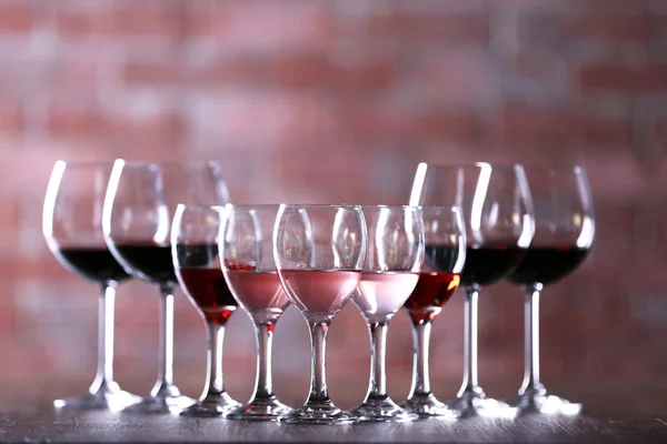 Wineglasses with white, red and pink wine on wooden table on wall brick background