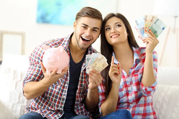 Happy couple sitting at home and counting money from the pig money box