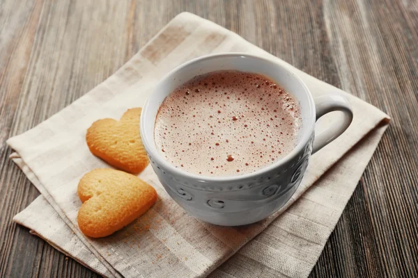 Cup of hot cacao with heart shaped cookies on cotton serviette