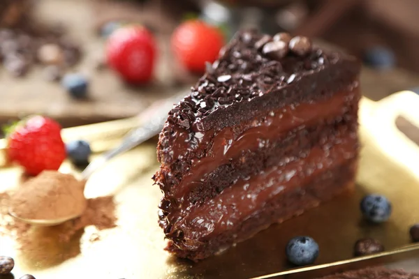 Chocolate cake with chocolate cream and fresh berries on tray, on wooden background