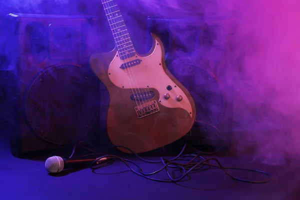 Big loudspeakers with electric guitar and microphone in dense smoke under purple light