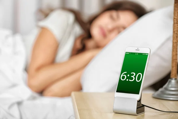 Beautiful young woman waking up with mobile alarm clock