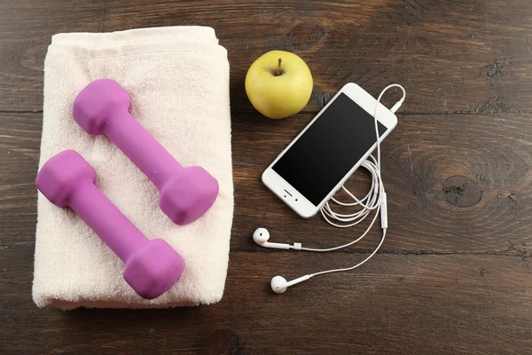 Sport equipment, towel and smart phone on wooden background