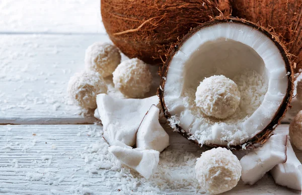 Candies in coconut flakes and fresh coconut on  light wooden background