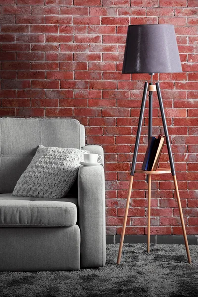 Comfortable sofa and lamp on brick wall background