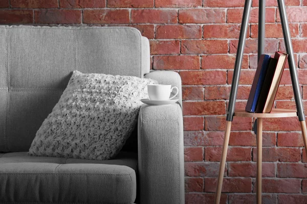 Comfortable sofa and lamp on brick wall background, close up