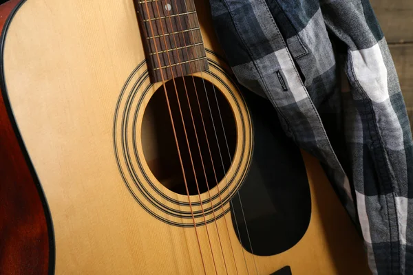 Acoustic guitar and blue checkered shirt against box with hay, close up