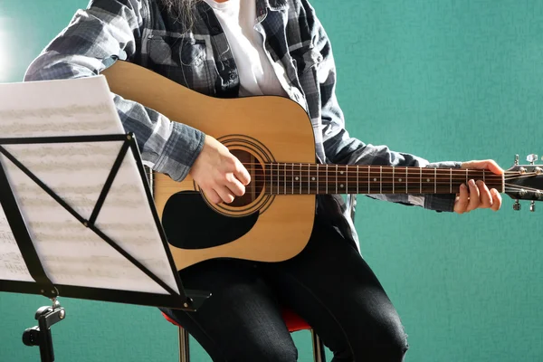 Musician plays guitar on blue background in studio with musical notes holder, close up