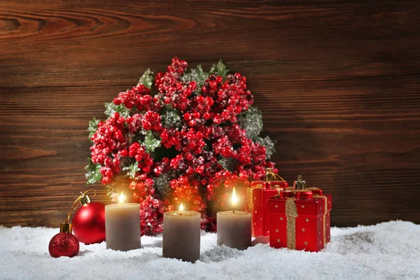 Three candles and toys with bouquet of holly berries in a snow over wooden background, still life