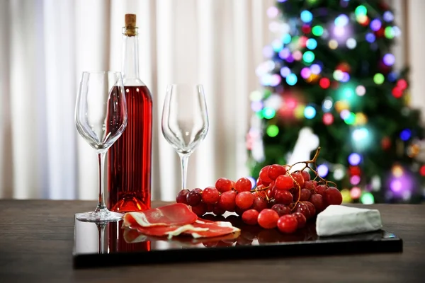 Pink wine bottle, two wineglasses, grape, slices of bacon and cheese on Christmas background
