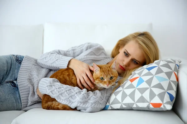 Young woman with red cat laying on sofa