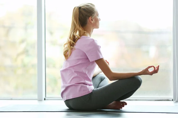 Young woman meditating against window