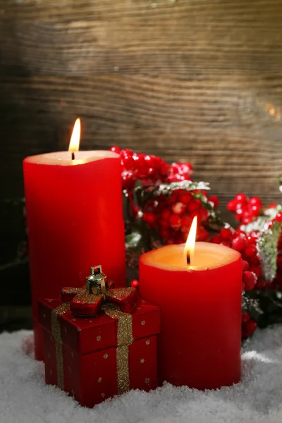 Burning candles, rowan and gift box with snow on wooden background