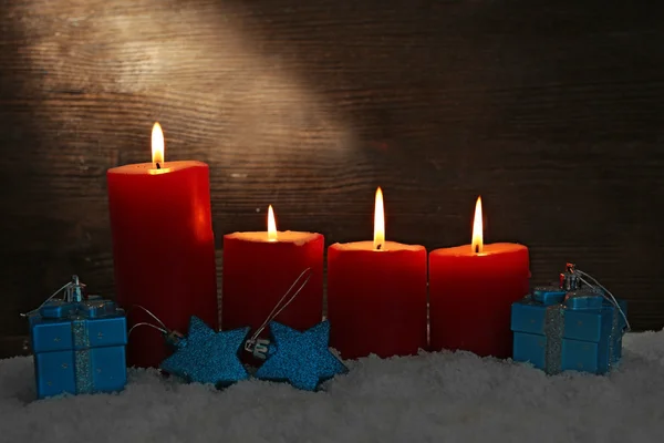 Burning candles and gift boxes with snow on wooden background