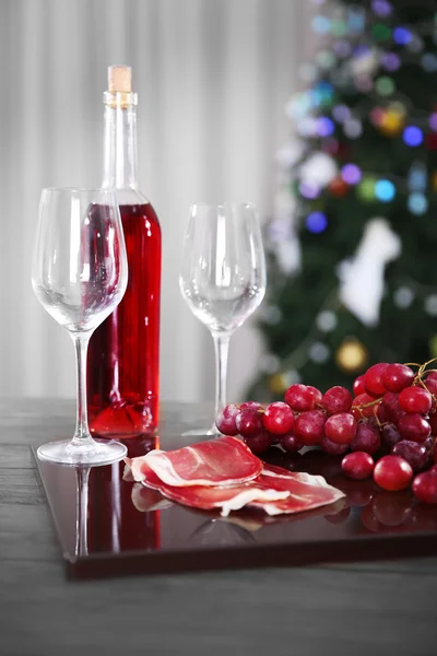 Pink wine bottle, two wineglasses, grape, slices of bacon and cheese on Christmas background