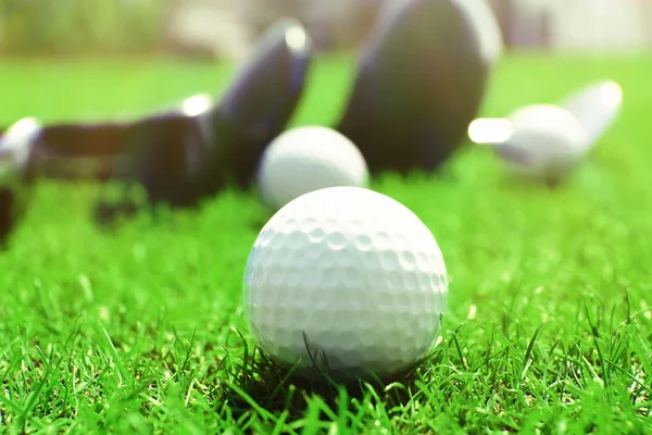 Different golf clubs in a row and balls on a green grass, close up