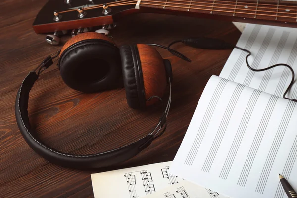 Guitar with earphones and music sheets on wooden background