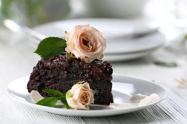 Piece of chocolate cake decorated with flowers on white wooden table