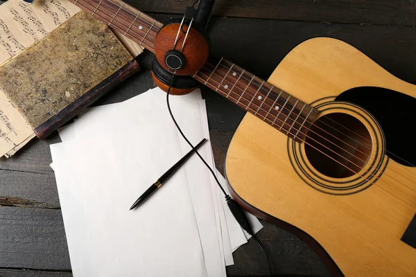 Acoustic guitar, headphones, musical notes and white papers on wooden background