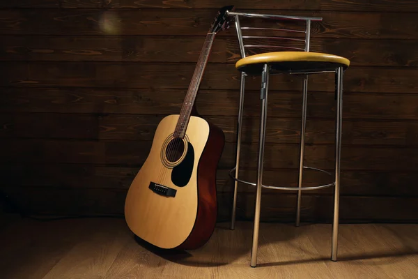 Acoustic guitar propped on wooden wall with bar stool in the room