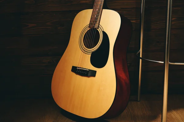 Acoustic guitar propped on wooden wall with bar stool in the room