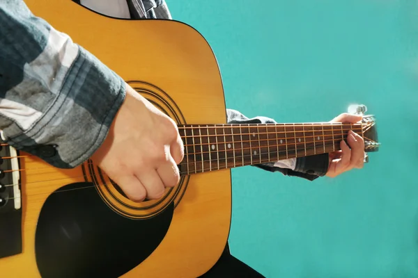 Musician plays guitar on blue background, close up
