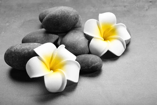Hot spa stones with flowers on grey background, close-up