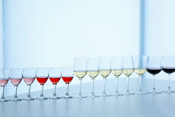 Wineglasses with white, red and pink wine on wooden table on bright background