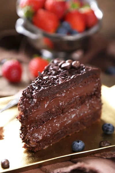 Chocolate cake with chocolate cream and fresh berries on tray, on wooden background