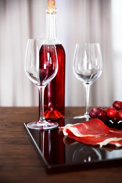 Pink wine bottle, two wineglasses, grape, slice of bacon on a table, still life
