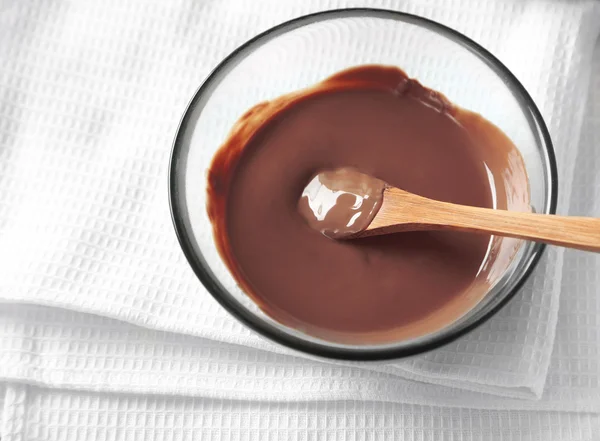 Melted chocolate in glass bowl, on wooden background