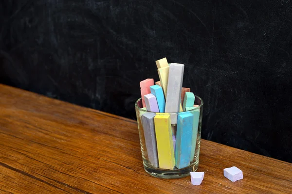 Glass of coloured chalk on desk in front of blackboard