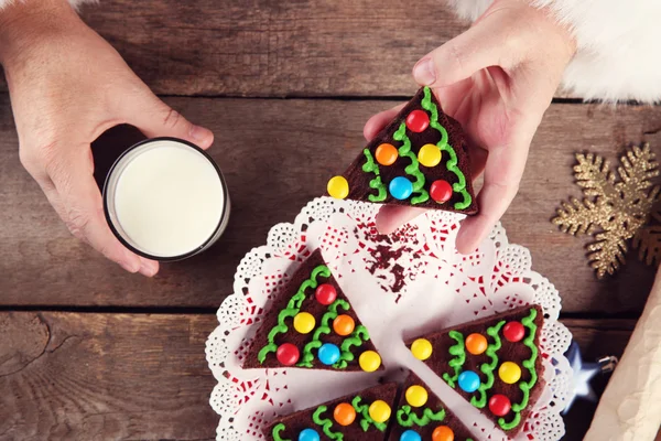Christmas concept. Santa have a meal. Santa hands take piece of chocolate cake and milk glass, close up