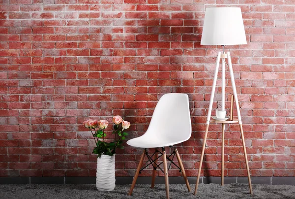 White modern chair with lamp and bouquet of roses on brick wall background