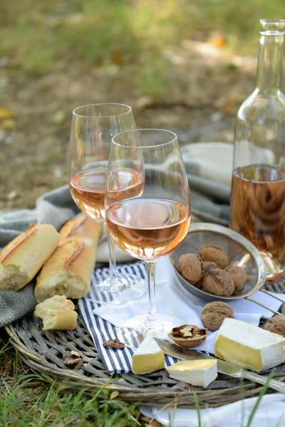 Picnic theme - rose wine, cheese, baguette and nuts on wicker tray, outdoors