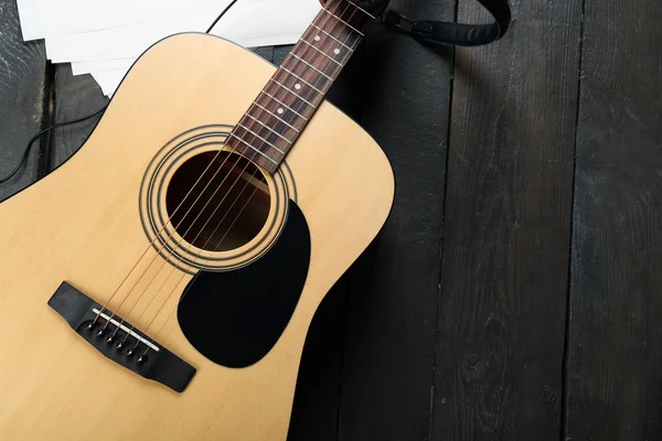 Acoustic guitar, headphones, musical notes and white papers on wooden background, close up