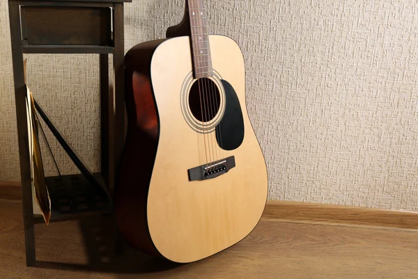 Acoustic guitar propped on wall with stool and headphones on it in the room, close up