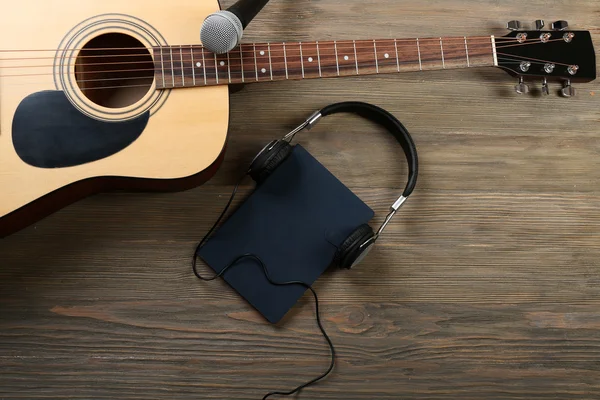 Acoustic guitar, headphones, notebook and microphone on wooden background