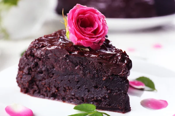 Piece of chocolate cake decorated with flowers on white wooden table